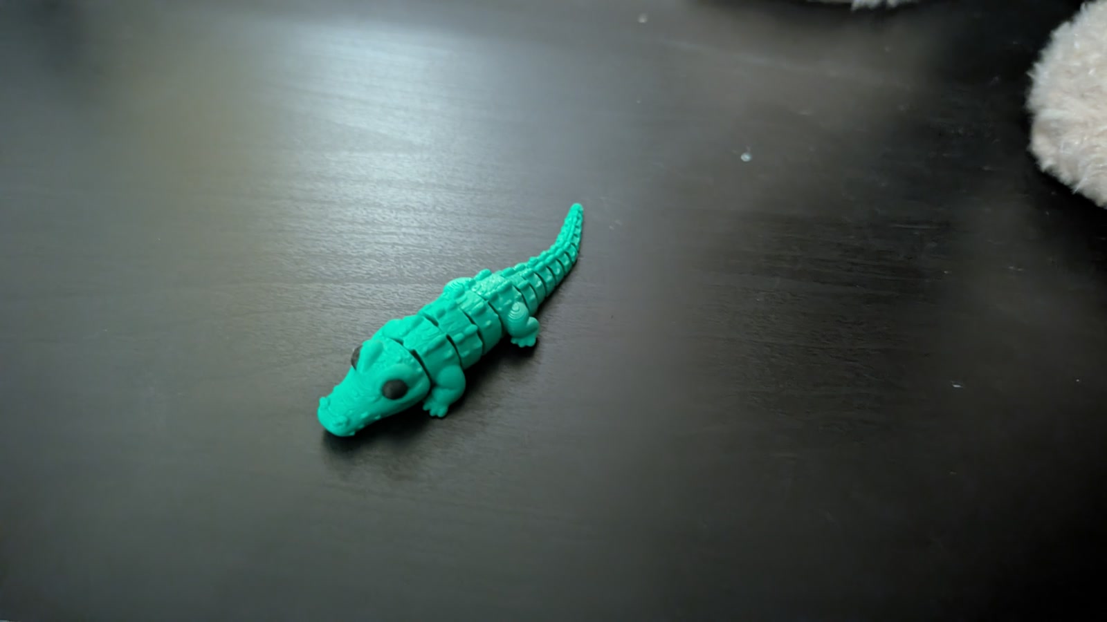 Small green articulated crocodile on a black shelf