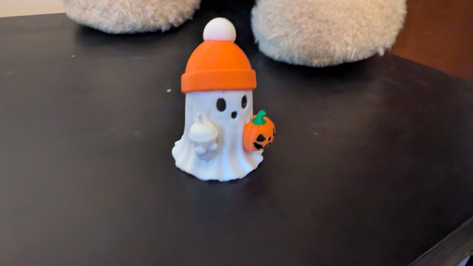 White printed ghost wearing an orange beanie and holding a tiny drink and pumpkin bucket