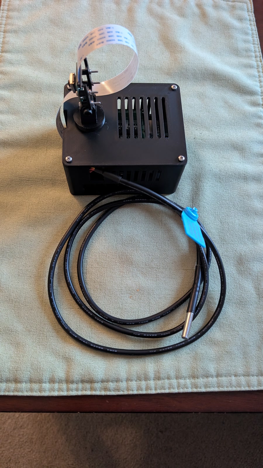 Black printed case housing a Raspberry Pi stack with a camera and connected sensors