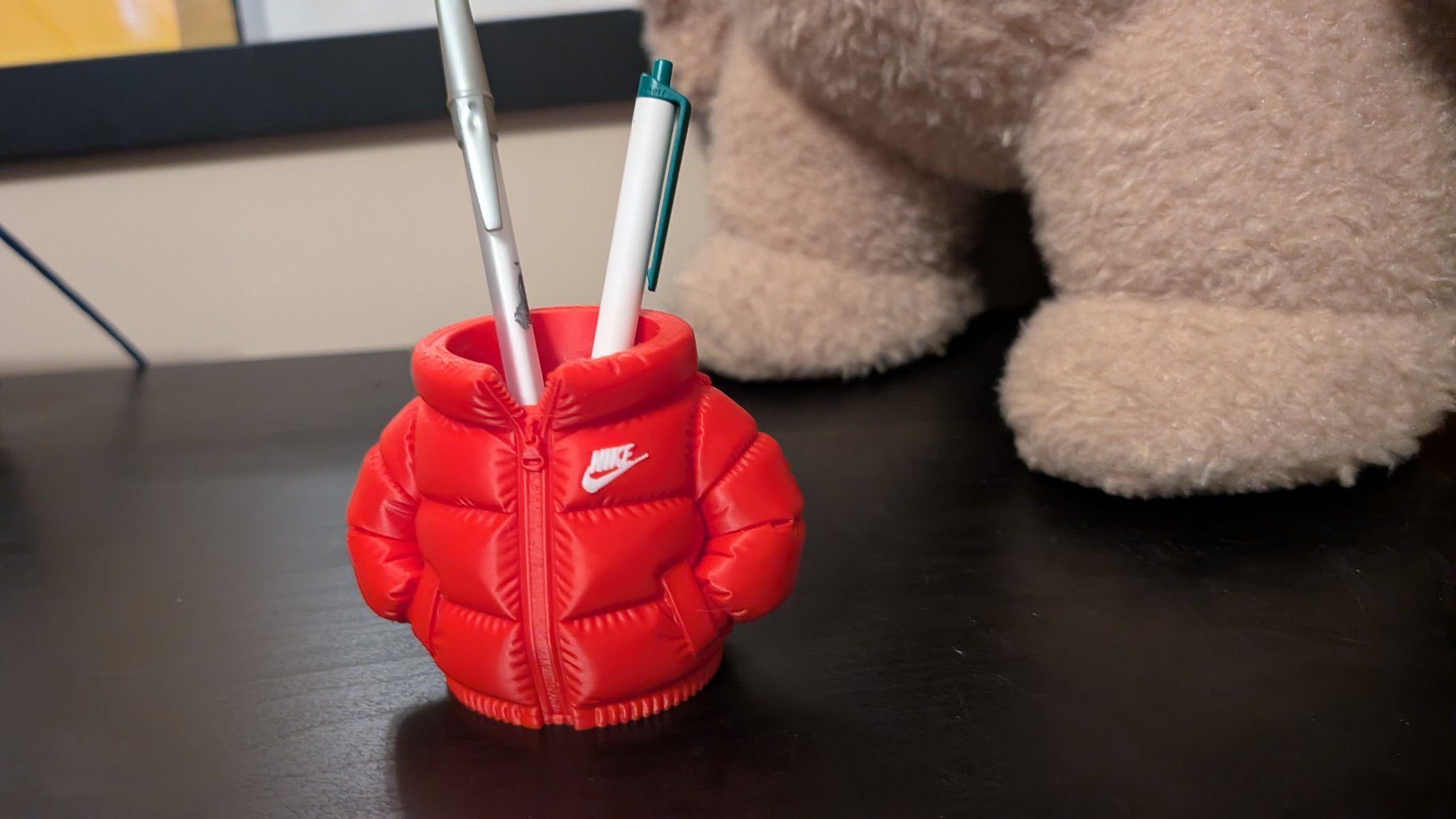 Red puffer-jacket-shaped pen holder with pens on a black shelf