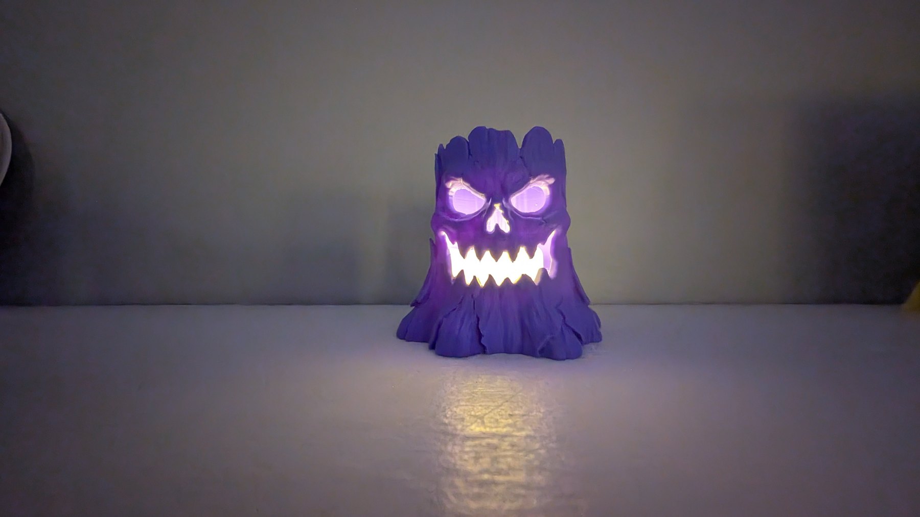 Purple printed spooky stump with its eyes and jagged mouth glowing in the dark