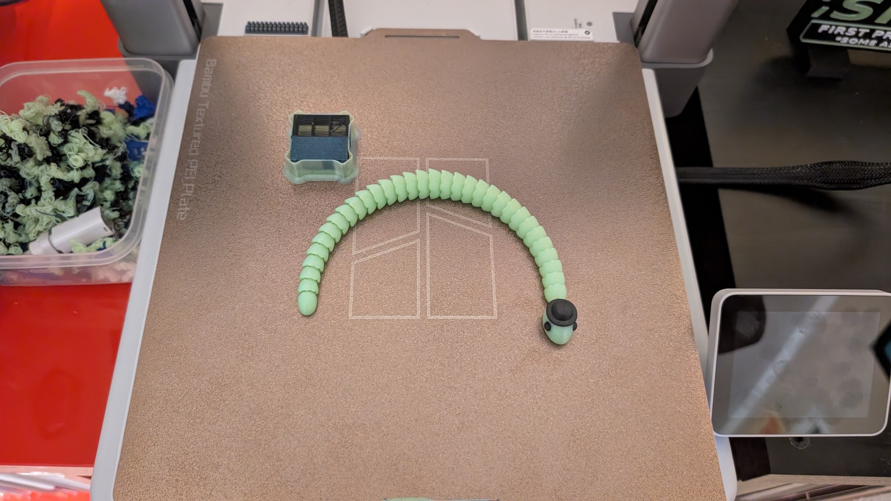 Green articulated snake with a black top hat on the build plate