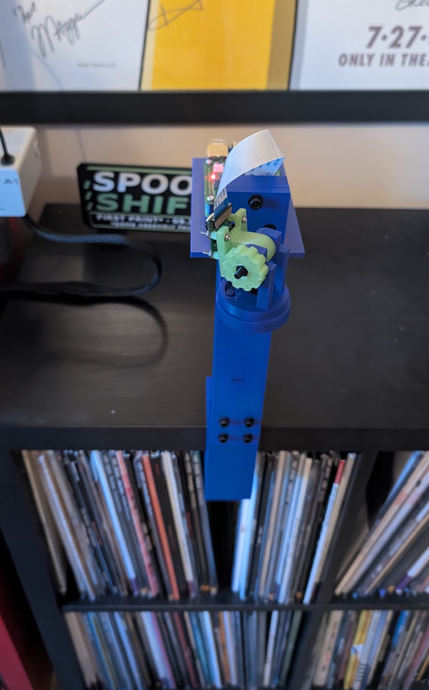 Blue printed camera mount clamped to the shelf with green adjustment knobs and the camera fitted