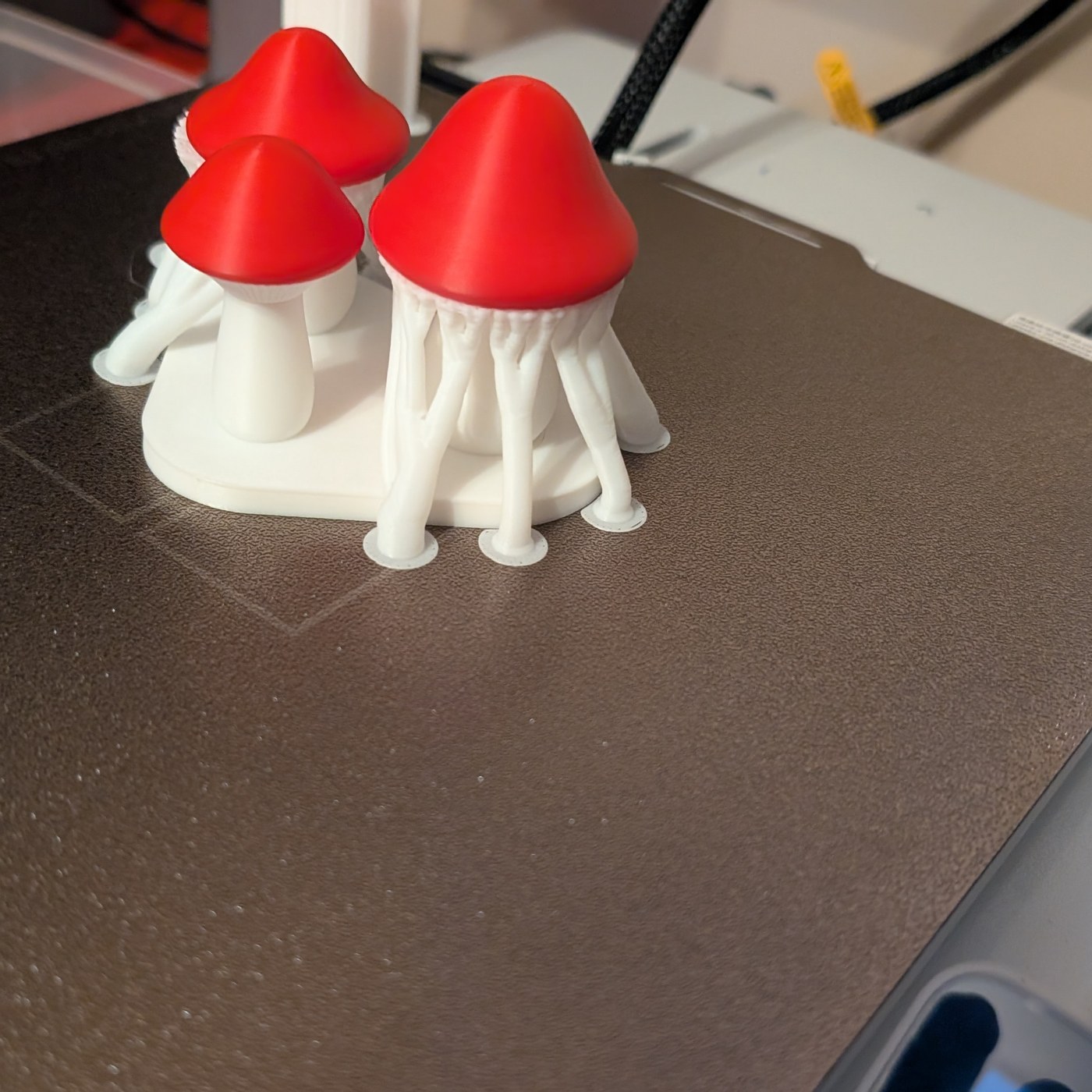 Three red-and-white printed mushrooms on the build plate, still surrounded by white tree supports